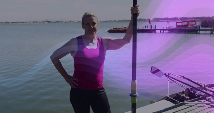 Standing woman wearing pink athletic top and black leggings on dock, holding rowing oar with shell - Powered by Adobe