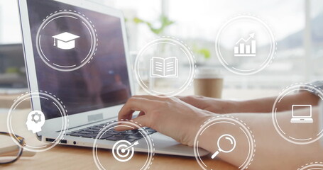Hands typing on laptop keyboard at desk by window, with coffee cup, eyeglasses and digital icons