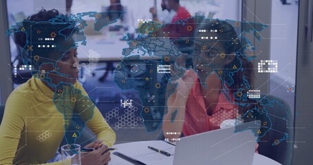 Discussing two women using laptop and documents in office, with digital world map overlay
