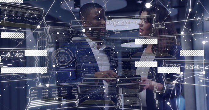 Two professionals wearing suits reviewing holographic data panels with tablet in server room