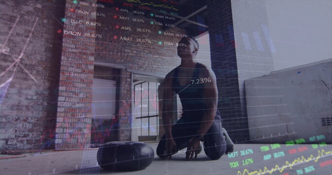 Kneeling male athlete in sportswear analyzing stock market overlays in loft gym, with weighted bags