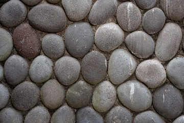 Abstract background texture of smooth, grey, and brown round river stones set in a wall. A natural,...
