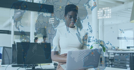Working data analyst typing on silver laptop in open-plan office, with digital world map overlay