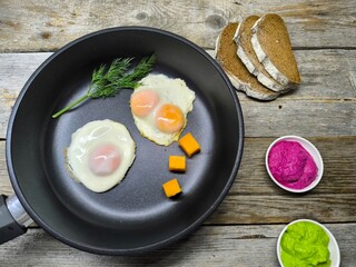 Top view of a frying pan with a breakfast of fried eggs and delicious bacon and various seasonings