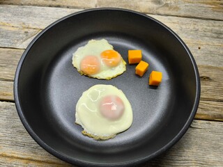 Two fried eggs in a black frying pan on a wooden table