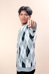 A young Asian man wearing a stylish gray argyle cardigan points his finger confidently at the...