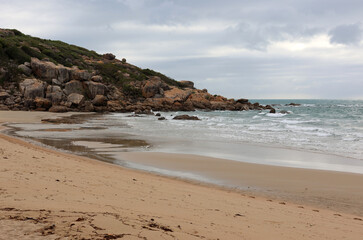 Rocky cliff and sandy beach under an overcast sky at Rose Bay near Bowen in Queensland, Australia