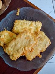 Close up of crispy fried tempeh on a glass plate, traditional Indonesian snack. Golden brown soybean cake fritters, popular street food, vegetarian protein, authentic Asian cuisine concept.
