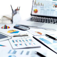 A top-down view of a cluttered desk filled with various business documents, charts, graphs, and devices. 