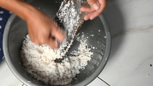 A woman squeezes coconut milk from fresh grated coconut.