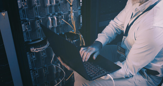 Cables, coding and hands with laptop, server room and network engineering with tech and electrician. Data center, technician and person with app for software upgrade, troubleshooting and online