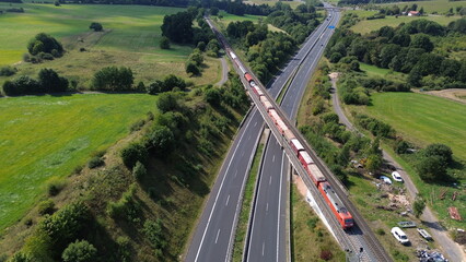 Aerial view of freight train crossing highway bridge through rural countryside with fields and forest