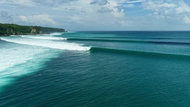 Drone aerial of surfers riding long left-hand waves at Impossibles, Bingin, Bali. The famous reef break peels across the coastline with turquoise ocean and tropical scenery.