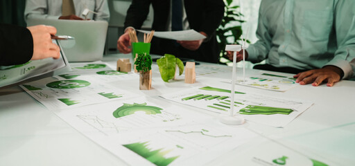 A professional business team engages in a productive discussion around charts and graphs in a modern office, surrounded by greenery and collaborative energy. SACTR