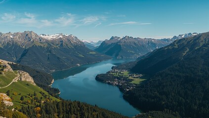 Obraz premium A breathtaking vista of a serene alpine lake nestled amongst snow-capped mountains, showcasing a vibrant green hillside and a deep blue water body.