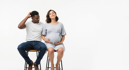 Pregnant woman with african american partner sitting on stools in studio. Interracial couple maternity session for diverse family planning and prenatal services