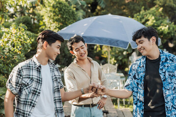 Three satisfied young Asian men fist bumping in mutual agreement and celebration while standing together in an outdoor garden setting.
