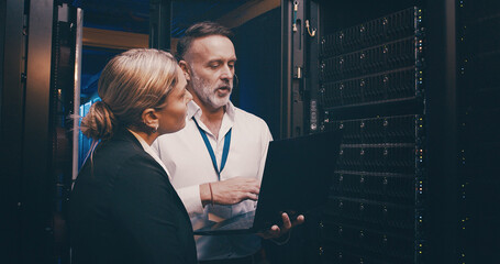 Server room, talking and people on laptop for technical support, network maintenance and database. IT technicians, team and man with woman on computer for diagnostics, system update and cybersecurity