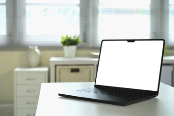 Laptop with blank white screen mockup on desk in bright office interior with natural light