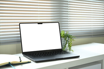 Fototapeta premium Workspace with laptop, notebook, and potted plant on white desk in natural light