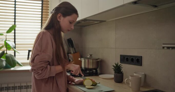 Side view of a focused teenage girl cutting a pear on a cutting board in the morning in the kitchen. Making a Healthy Breakfast and Fruits