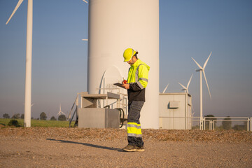 Engineer working in front of wind turbines for checking wind turbines of the field during beautiful sunset. Alternative energy concept.