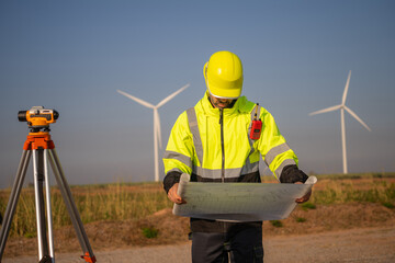 Engineer working in front of wind turbines for checking wind turbines of the field during beautiful sunset. Alternative energy concept.