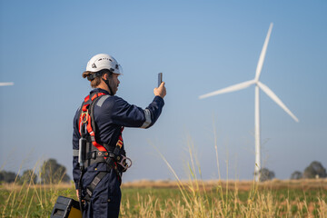 Engineer working in front of wind turbines for checking wind turbines of the field during beautiful sunset. Alternative energy concept.