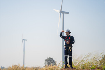 Engineer working in front of wind turbines for checking wind turbines of the field during beautiful sunset. Alternative energy concept.