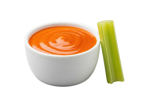 Sleek white ceramic ramekin brimming with rich orange Buffalo wing sauce, beside a crisp green celery baton, on a seamless transparent background, high-key studio shot, commercial food concept
