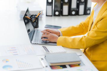 Focus and Functionality: A professional in a yellow jacket is engrossed in work on a laptop at a...