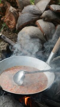 Indonesian woman preparing seblak over charcoal fire in a bamboo saung near rice fields. Traditional cooking method and countryside atmosphere.