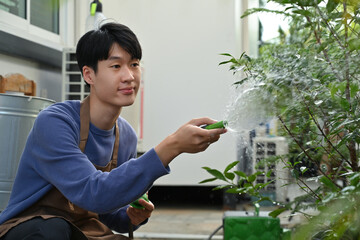 Gardener tending to potted greenery with hose in a backyard garden