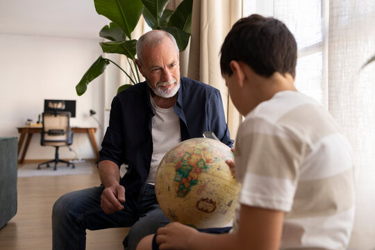 Grandfather teaching grandson geography with globe indoors