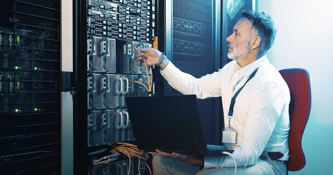 Cable, technician and laptop with man in server room for hosting database, inspection and cybersecurity. Hardware storage, cloud computing and system backup with mature person in data center
