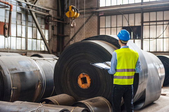 Employee inspecting rubber roller in industrial hall with safety gear