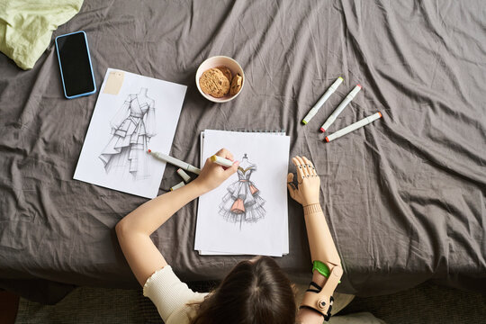 Creative girl drawing fashion sketches with prosthetic arm at home