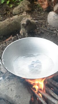 Indonesian woman preparing seblak over charcoal fire in a bamboo saung near rice fields. Traditional cooking method and countryside atmosphere.