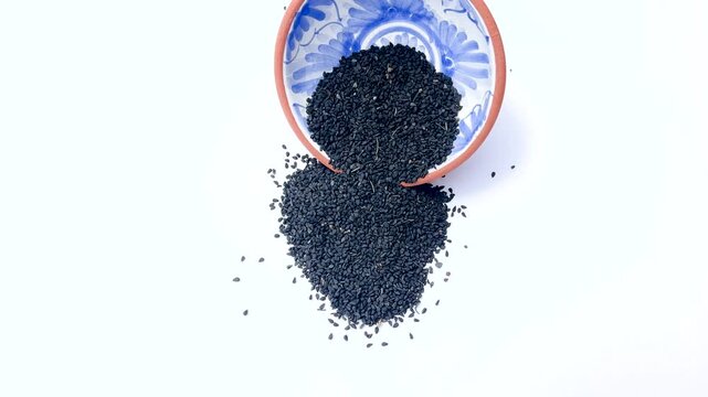 Nigella Sativa Black Seeds Spilled from Clay Bowl on White Background