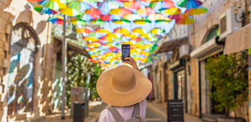 Back view of female traveler taking pictures of landmarks on her phone in the historic city of...