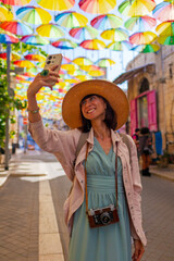 Girl Tourist on an excursion stands on the street with hanging umbrellas and takes pictures....