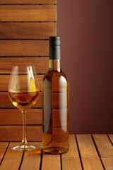 Bottle and glass of white wine on a wooden background.