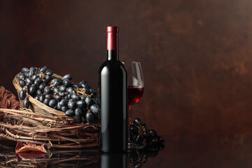Glass and bottle of red wine with blue grapes on a black reflective background.