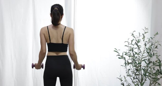 Woman from the back, lifting dumbbells, symbolizing fitness and a commitment to a healthy lifestyle for overall wellness, a healthy and fit lifestyle. Good habits for a balanced life
