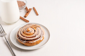 Delicious homemade cinnamon roll bun or swirl decorated with sugar icing served on plate on white...