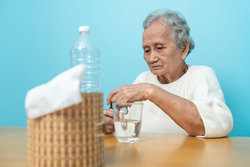 An elderly Asian woman pours medicine from a plastic bottle to prepare to take medicine.