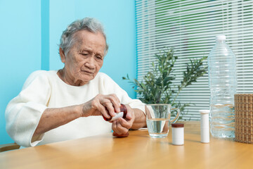 An elderly Asian woman pours medicine from a plastic bottle to prepare to take medicine.