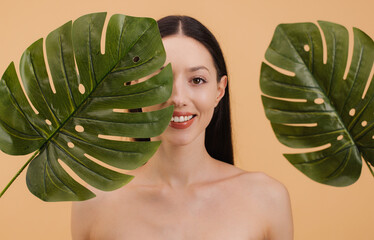 Beautiful smiling woman holding tropical leaves in front of her face. Beauty concept.