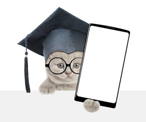 Funny smart college graduate kitten holds big smartphone with white blank screen in it paw, showing...