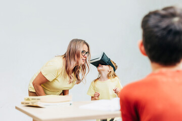 Teacher guiding schoolgirl exploring virtual reality technology in classroom